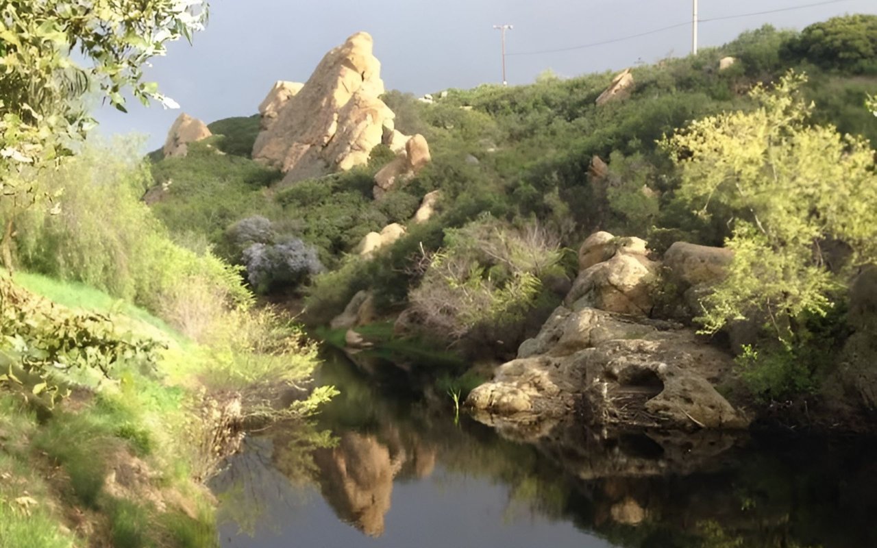 Rock formations and green chaparral hills reflected in a still creek in the Santa Monica Mountain Range.