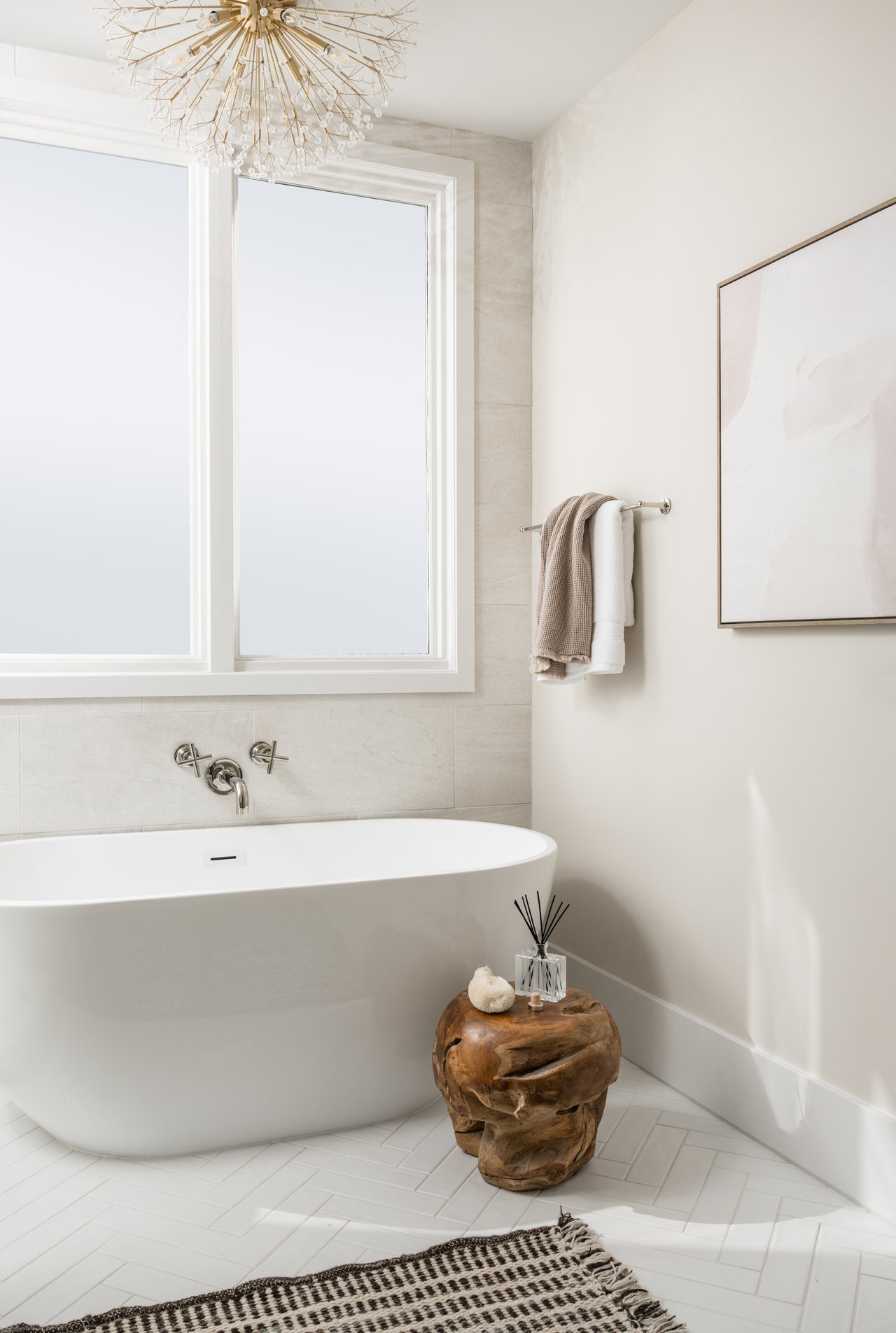 Bright bathroom with a freestanding tub beneath a large window and chandelier overhead.