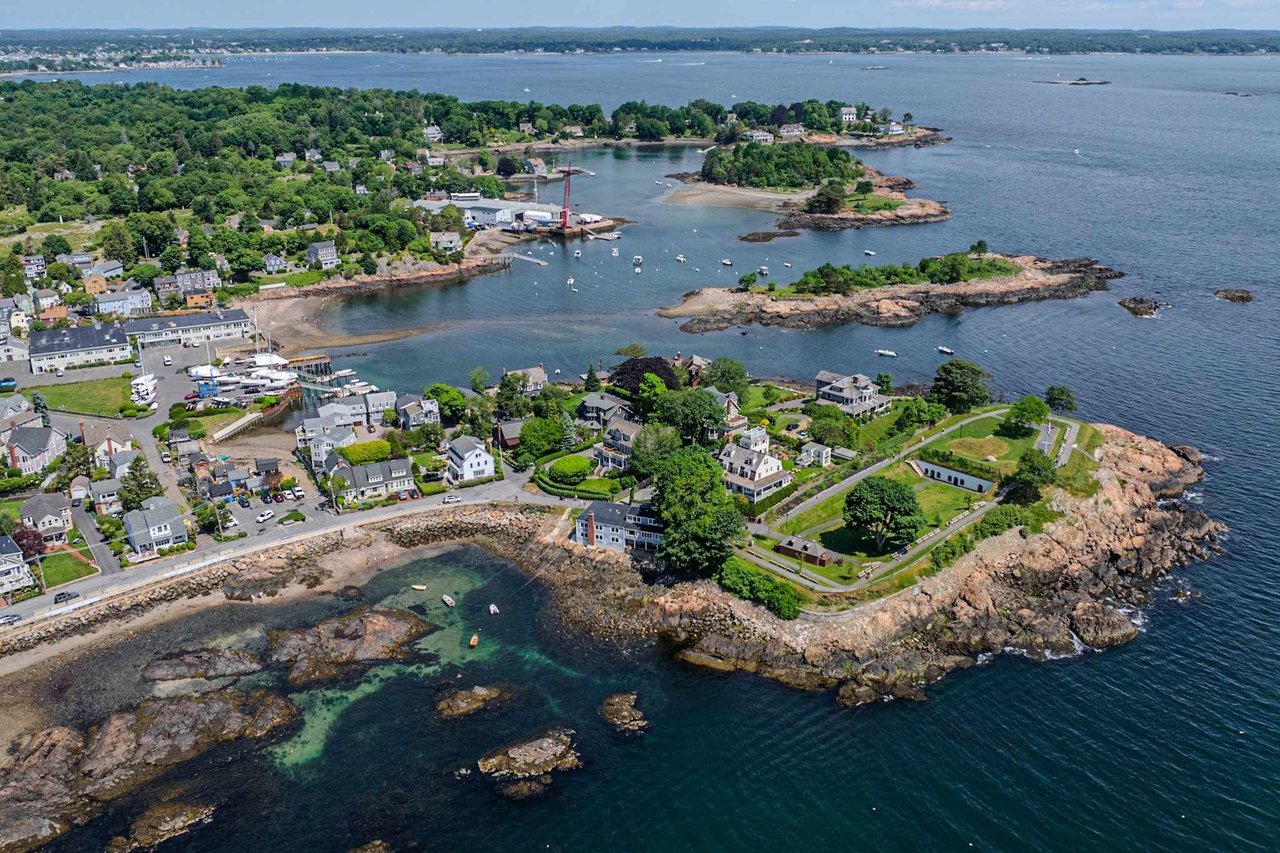 Aerial view of waterfront homes and rocky shores beside small harbors and boats.