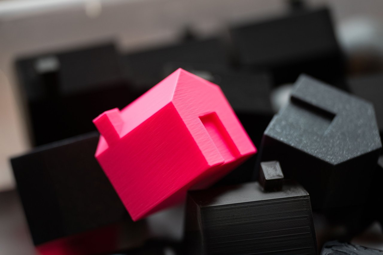 Bright pink miniature house among several black house-shaped models.
