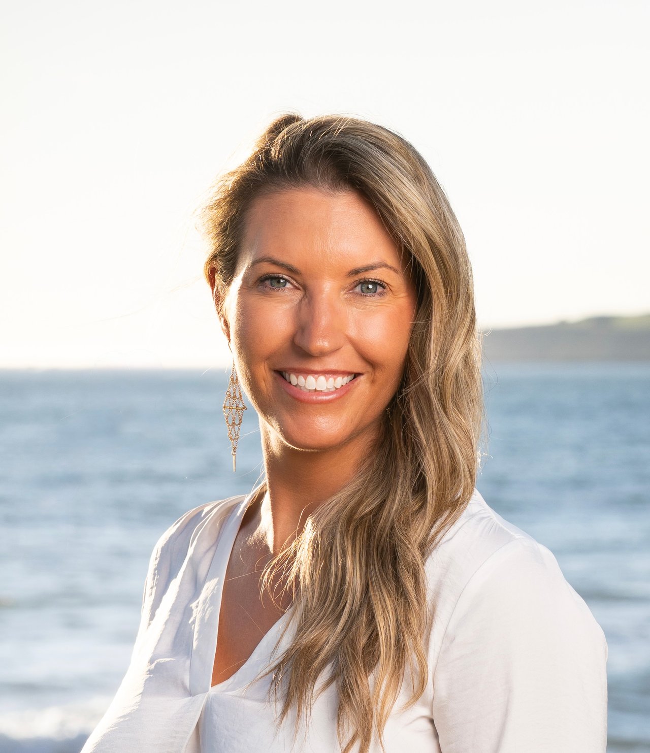 Melanie Haugen, Director of Operations at Ocean Element Real Estate, smiling on a beach in Half Moon Bay along the San Mateo County Coastside