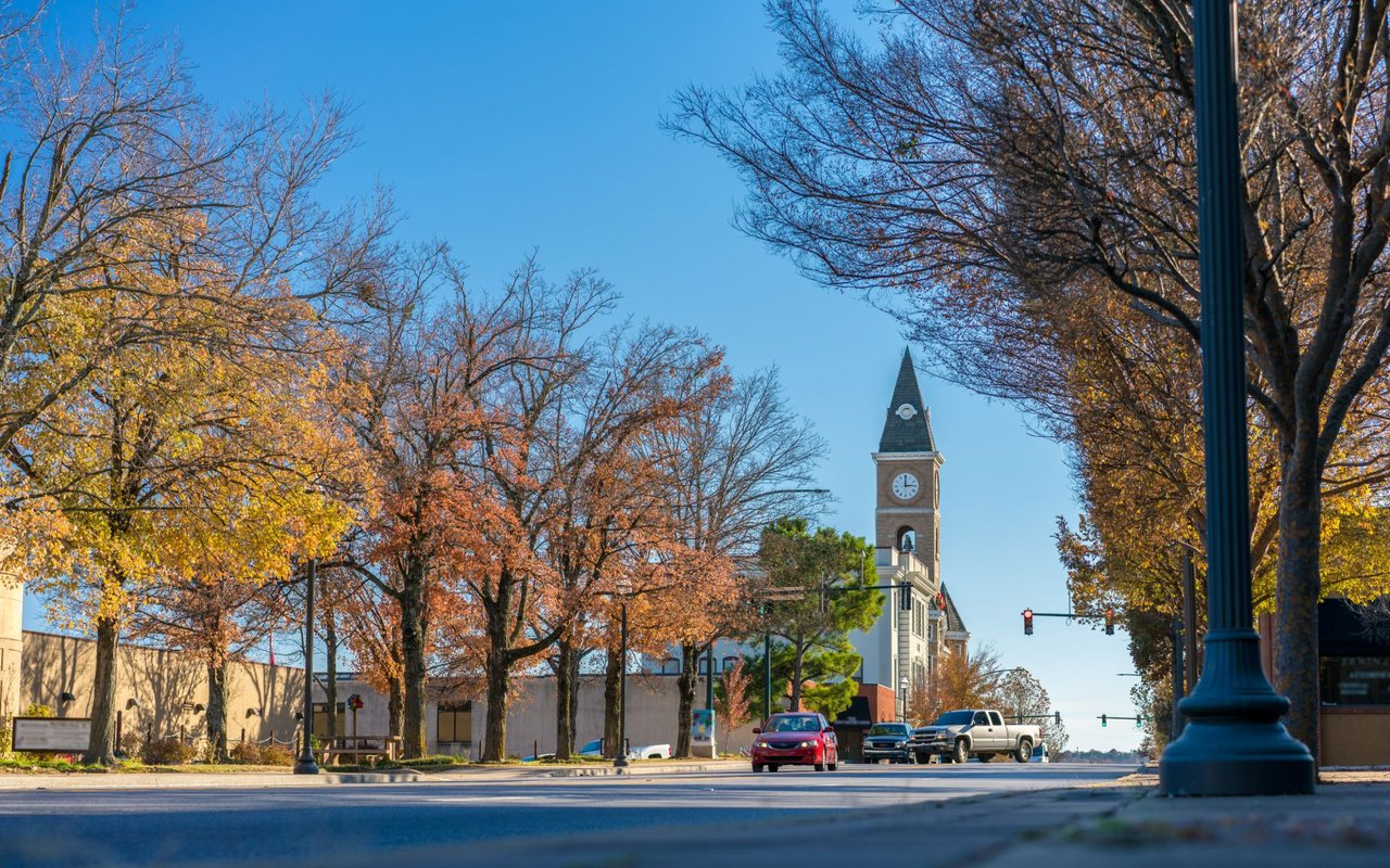 Fayetteville street with a clock tower, autumn trees, and passing cars.