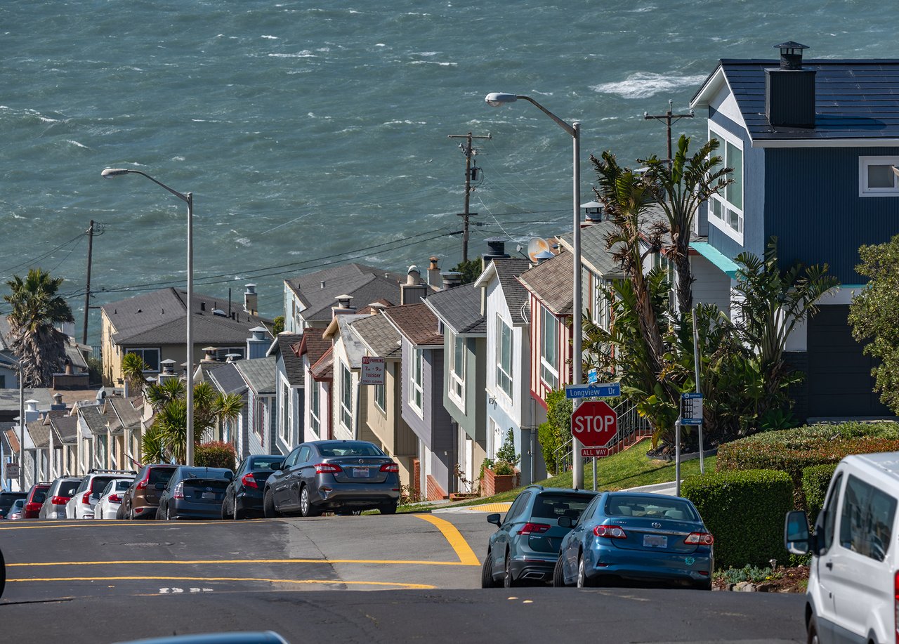 Coastal neighborhood street descending past closely spaced homes toward the ocean.