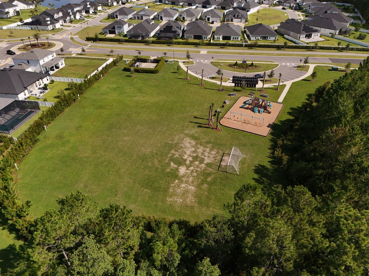 Aerial view of a neighborhood park with a playground, soccer goal, and surrounding homes.