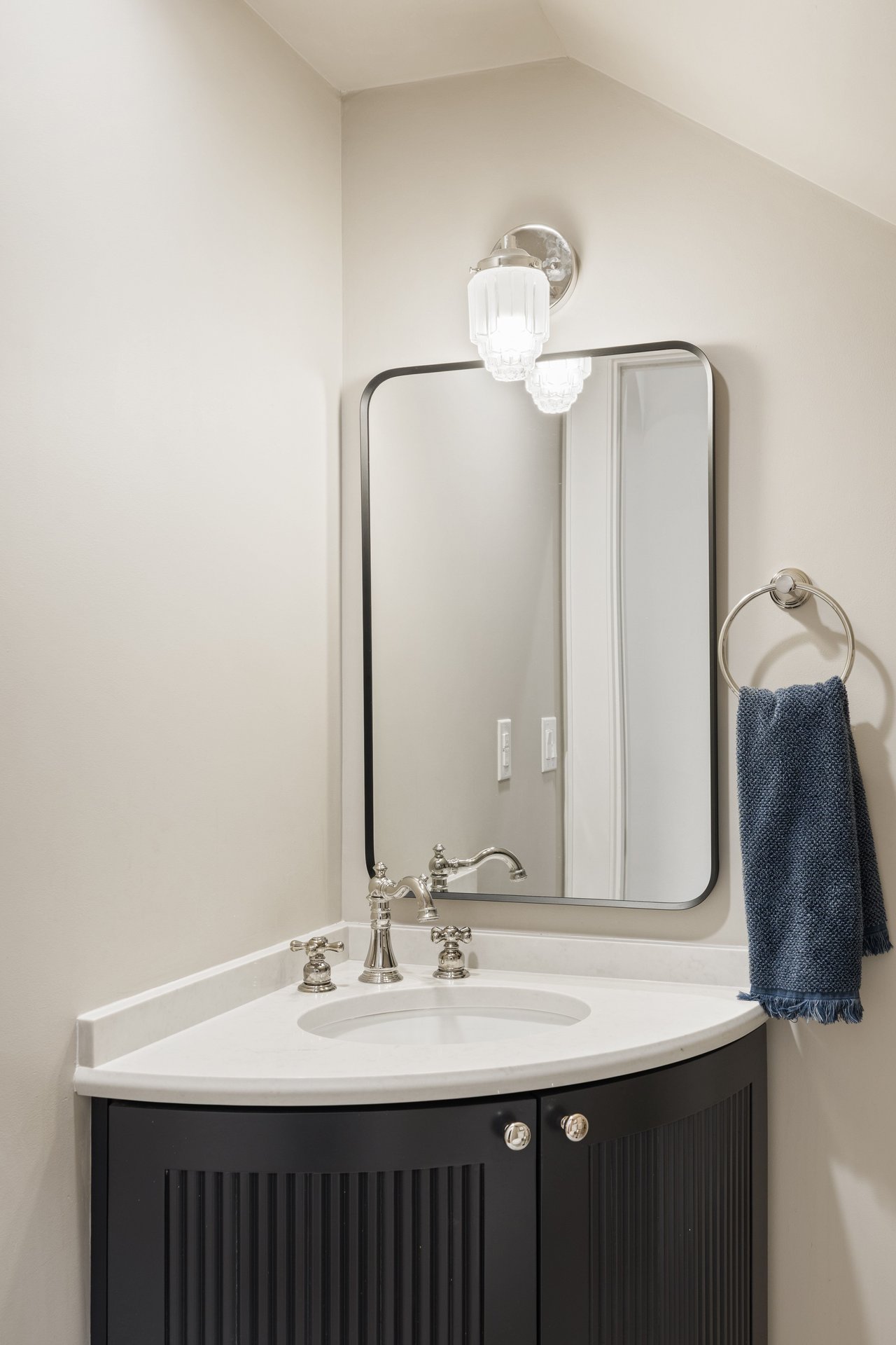 Bathroom vanity with a white sink, dark fluted cabinet, black-framed mirror, and blue hand towel.