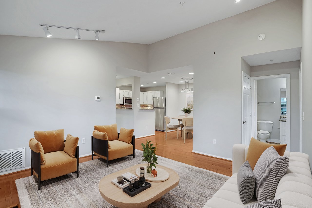 Furnished living room with tan armchairs, white sofa, and open kitchen and dining area.