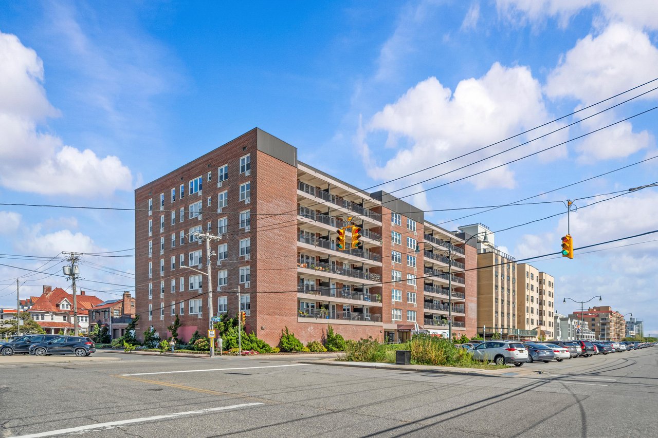 Red-brick cooperative apartment building with stacked balconies on a busy city corner.