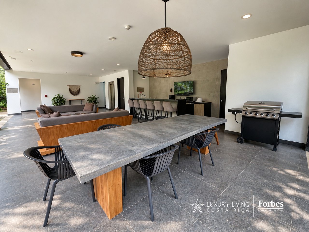 Furnished lounge and dining area with a long stone table, bar seating, and a built-in grill.