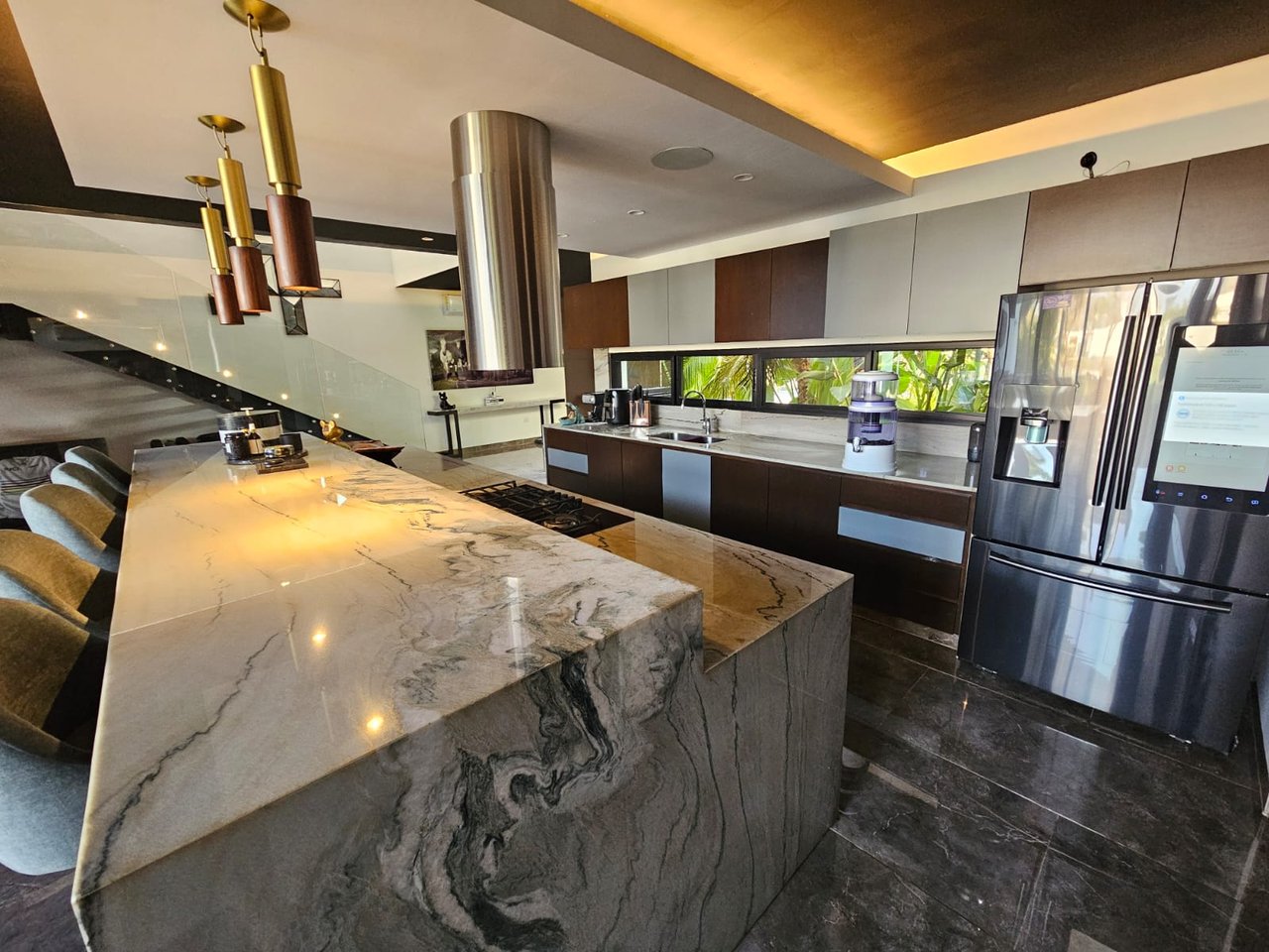 Modern kitchen with a dramatic veined marble island, stainless steel appliances, and a window facing tropical greenery.