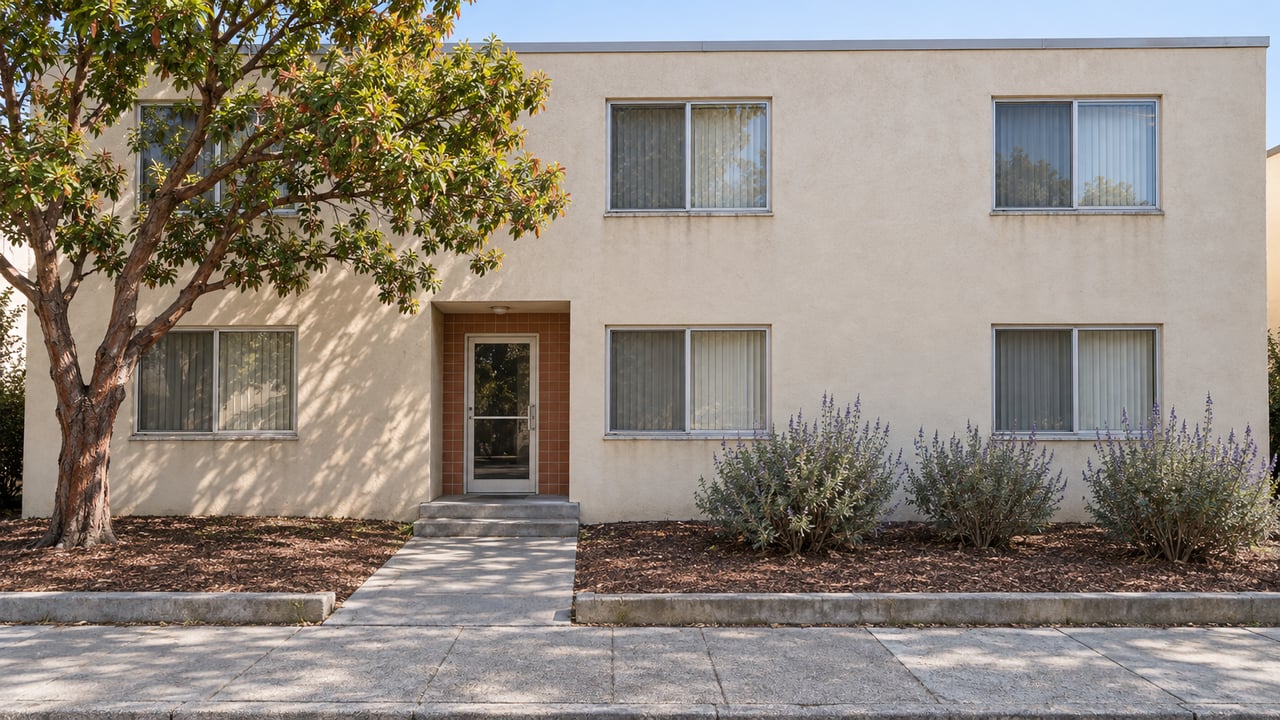 Sunlit two-story stucco apartment building with six windows, a terracotta-tiled recessed entry and a small planted setback.