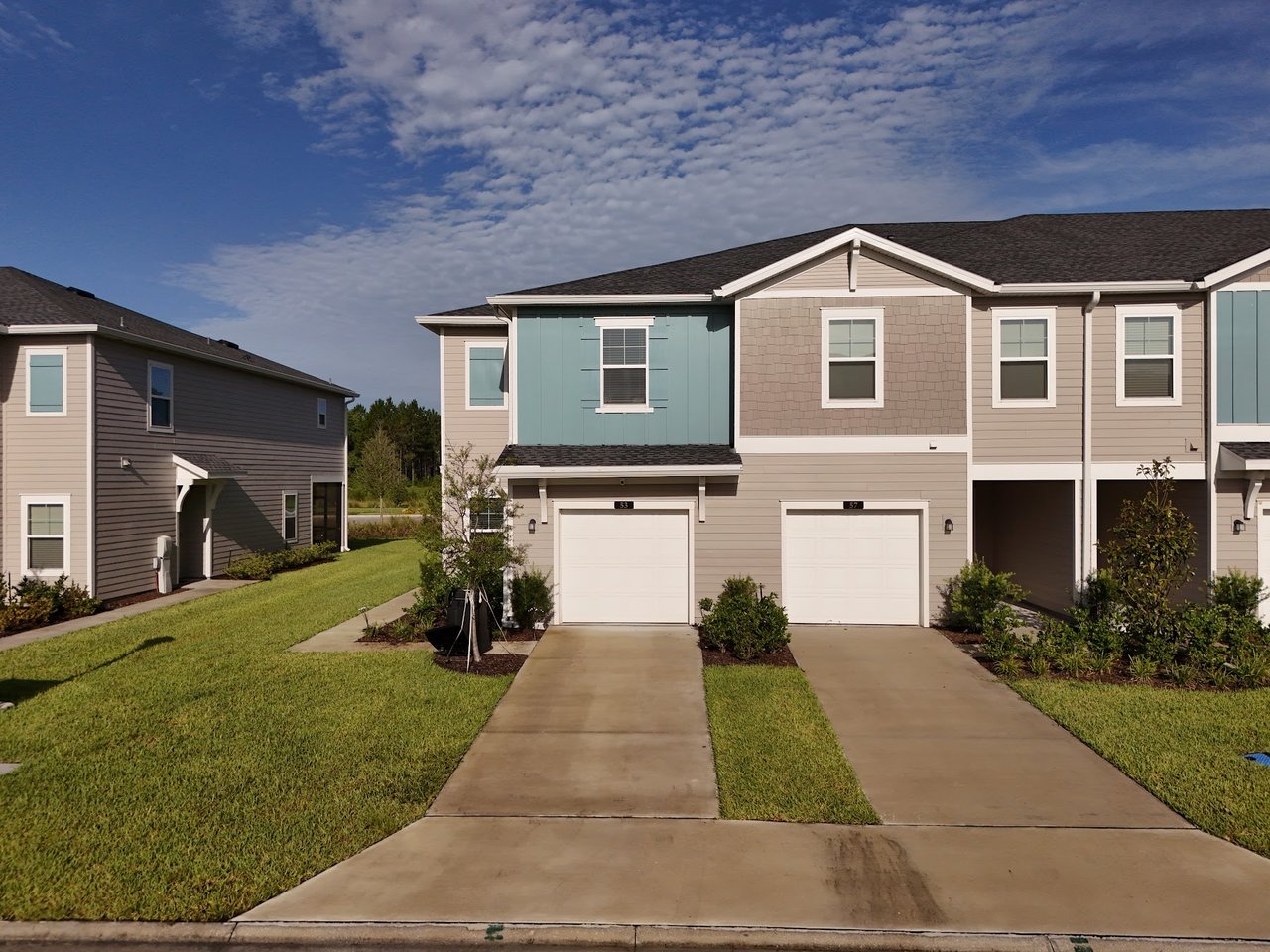 Attached two-story townhomes with gray and teal siding, white garage doors, and front lawns.
