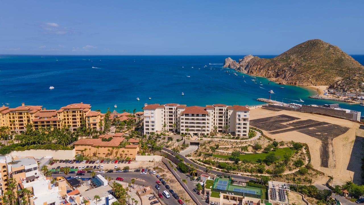 Beachfront condominiums beside a blue bay, with boats offshore and a rocky headland.