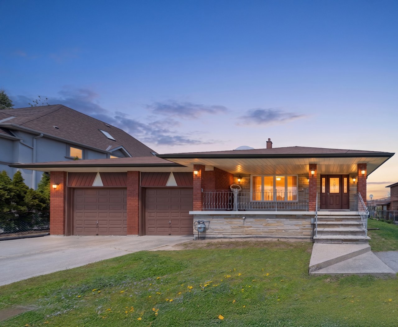 Brick house with a broad covered porch, two garages, and warmly lit windows at dusk.