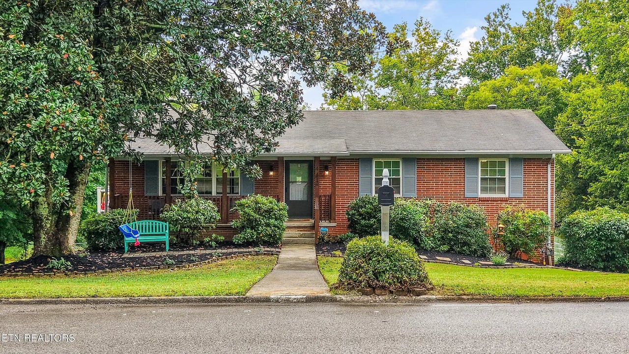 Red-brick ranch home with a covered porch, blue shutters, and a landscaped front yard.