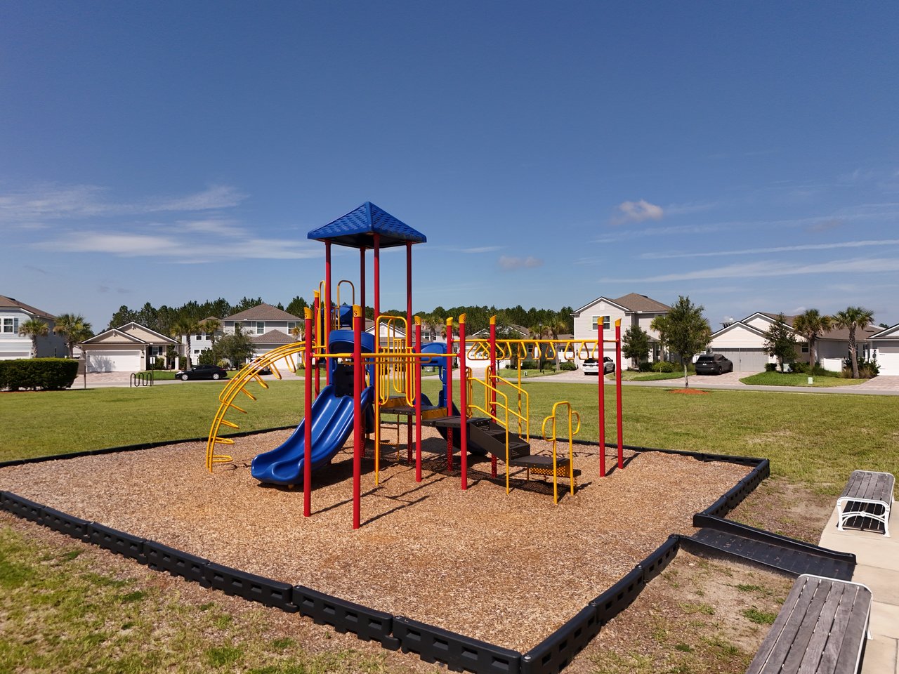 Neighborhood playground with blue slides and colorful climbing equipment, surrounded by homes.