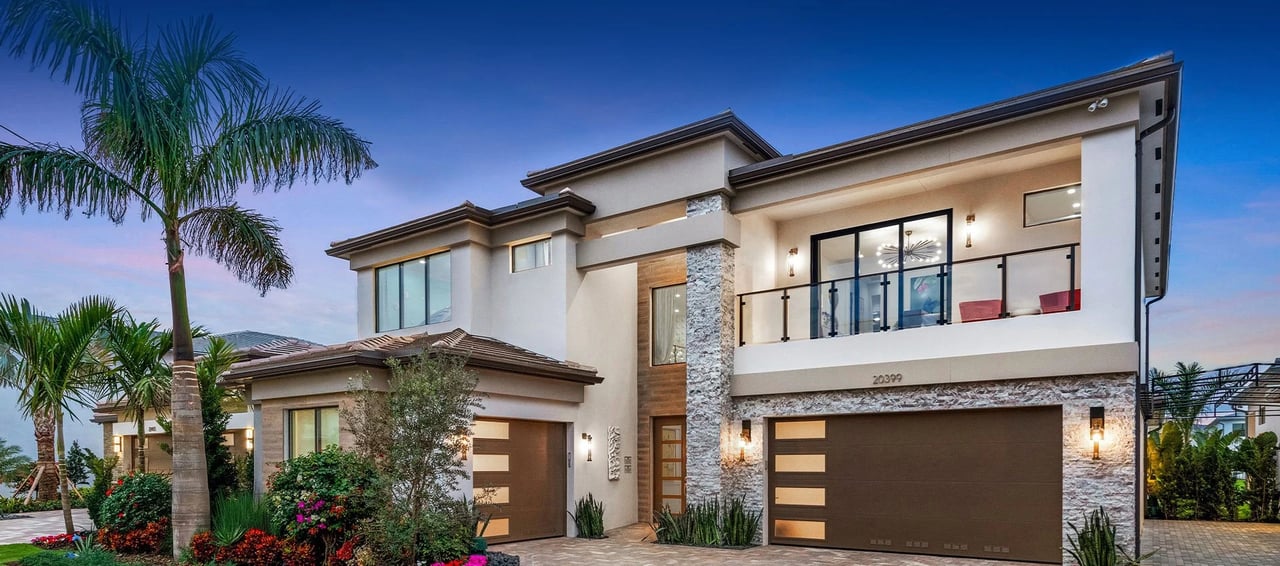 Modern two-story Lotus Edge home with an upper balcony, stone accents, and palm landscaping.
