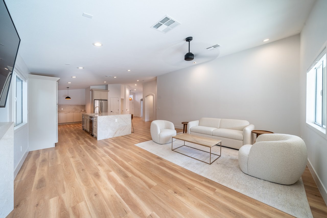 Open-plan kitchen and living room with a marble island, light wood floors, and cream seating.
