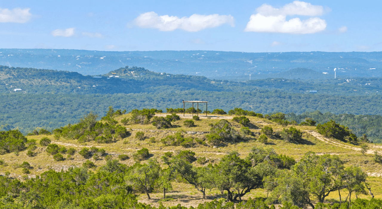 Wooded Hill Country acreage with a rocky ridge, open shelter, and distant hills.