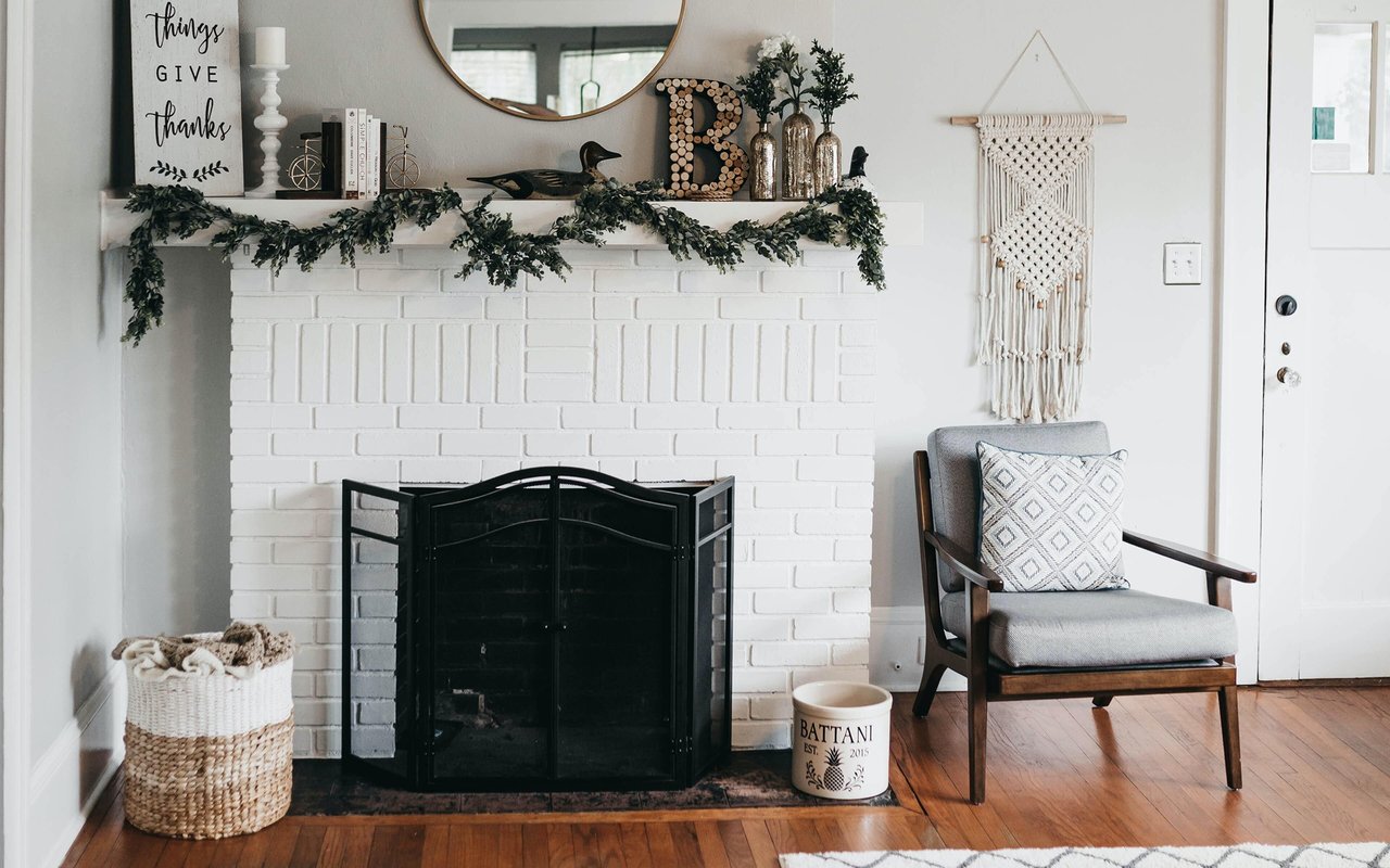 Furnished living room with a white brick fireplace, decorated mantel, and gray armchair.