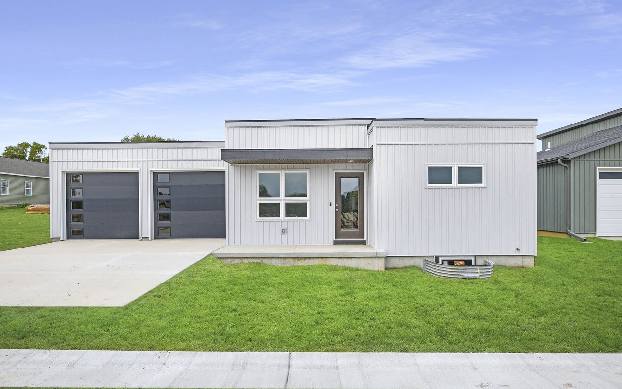Modern white flat-roof home with two dark garage doors and a broad concrete driveway.