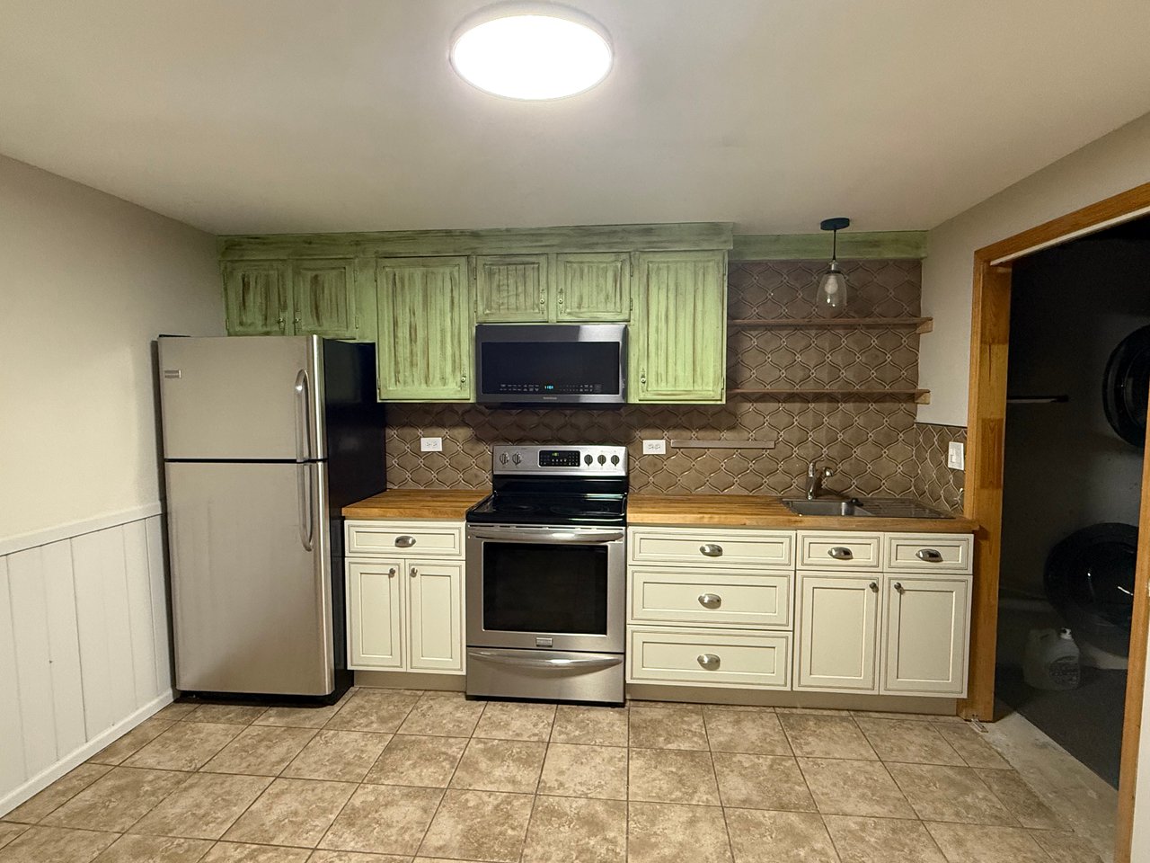 Kitchen with green upper cabinets, cream lower cabinets, patterned backsplash, and stainless steel appliances.