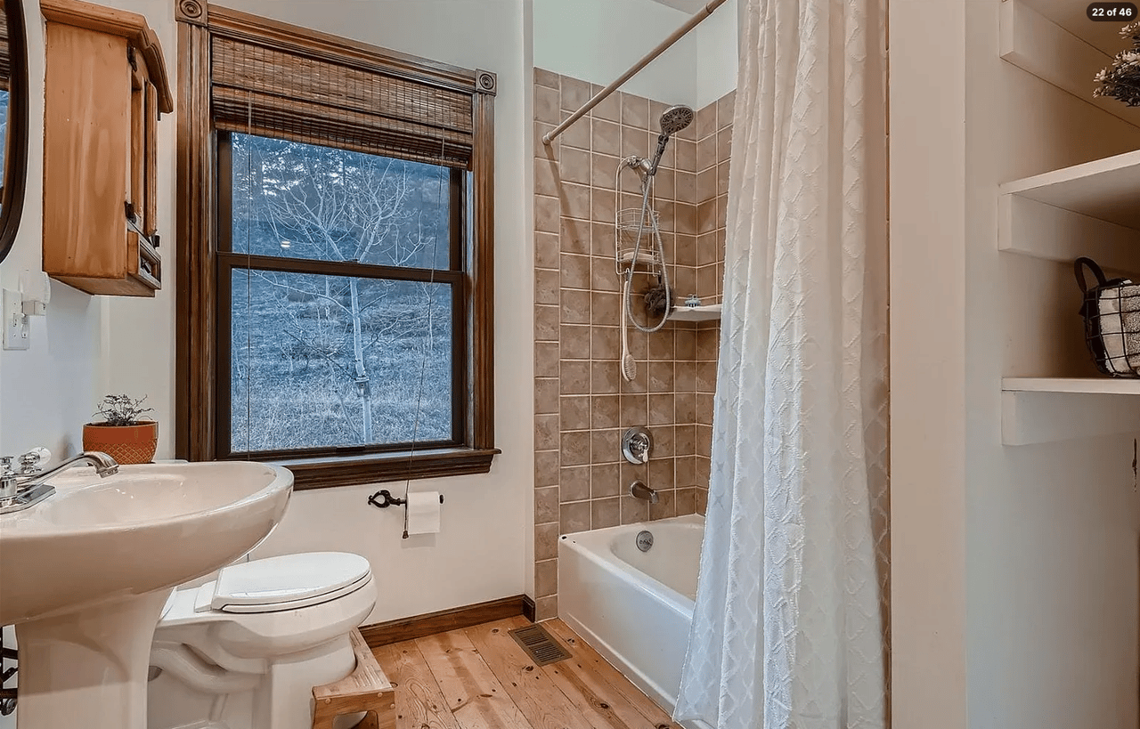 Bathroom with a tiled tub-shower, pedestal sink, and wood-trimmed window.