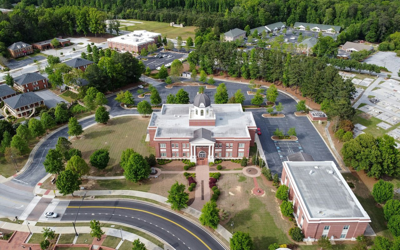 Aerial view of a red-brick campus centered on a cupola-topped building, surrounded by parking lots and trees.