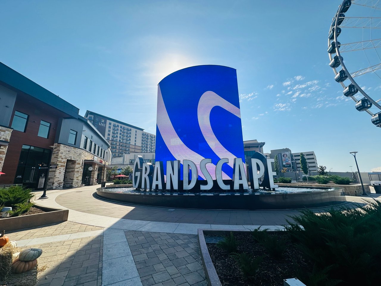 Grandscape plaza with its large blue sign, surrounding shops, and a Ferris wheel.