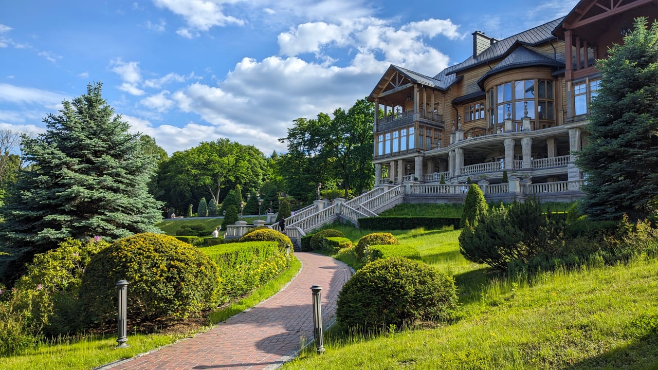 Luxury home with timber siding and stone columns, approached by a winding brick path through landscaped gardens.