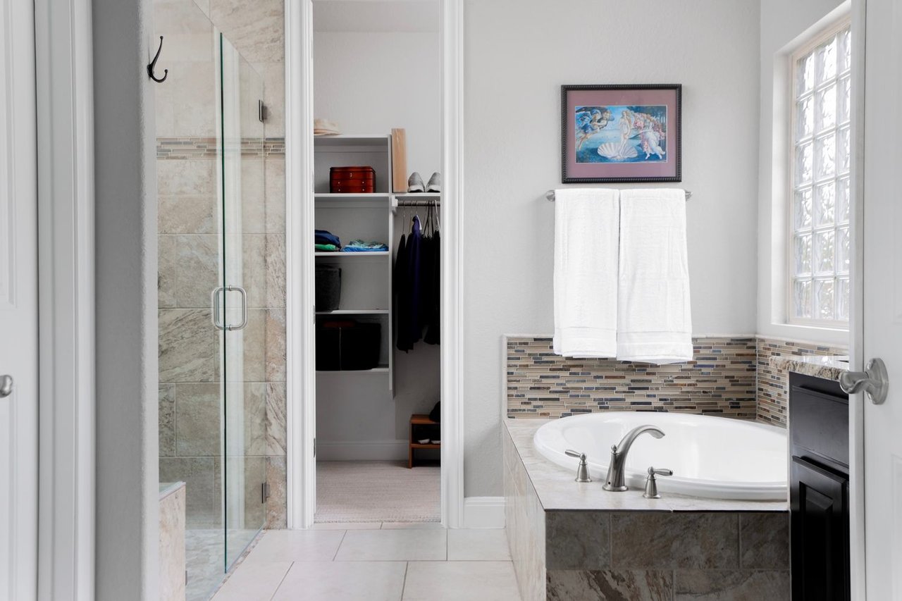 Bathroom with a built-in soaking tub, glass shower, and doorway to a walk-in closet.