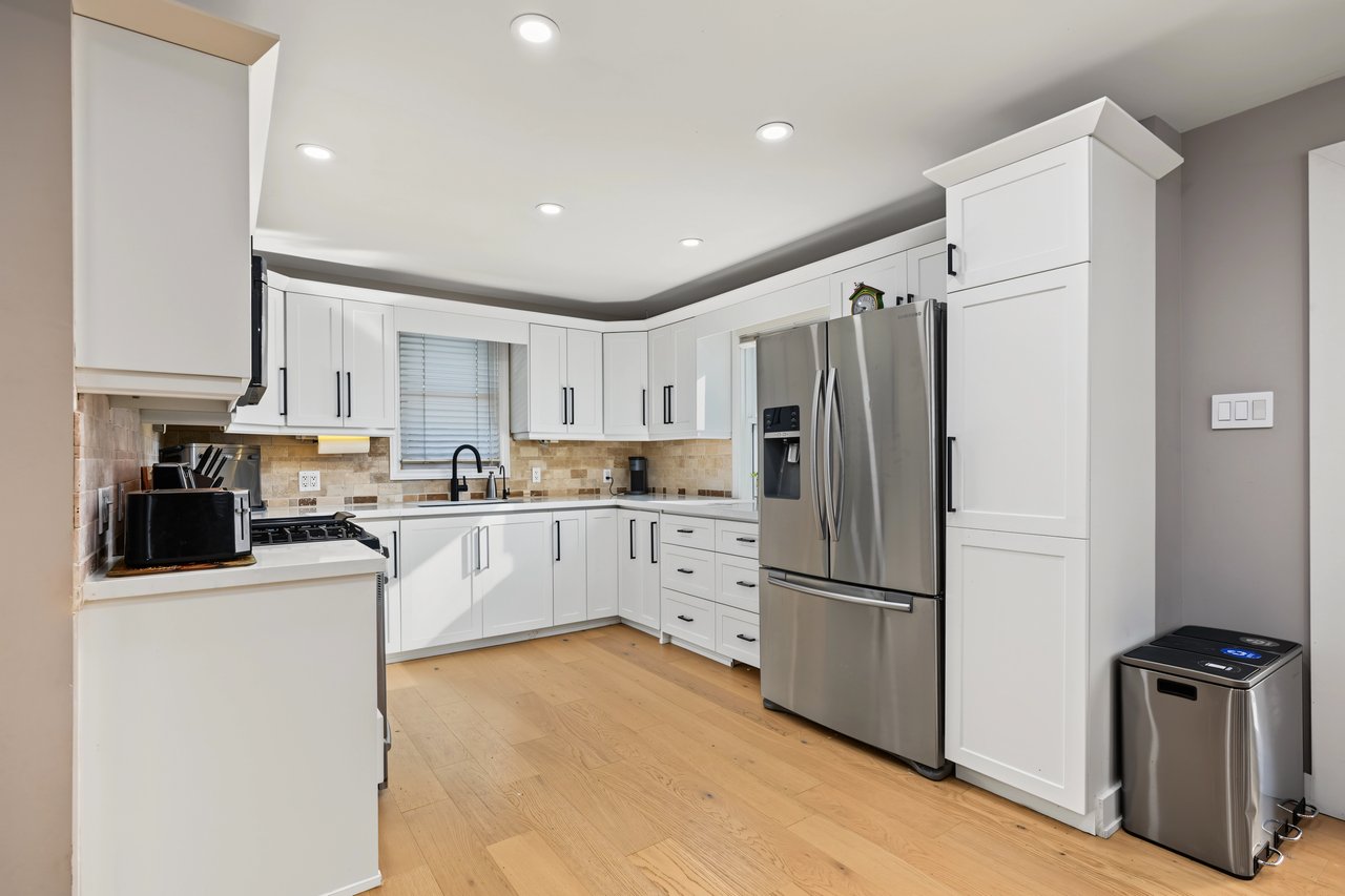 Kitchen with white cabinets, stainless steel appliances, beige tile backsplash, and light wood flooring.