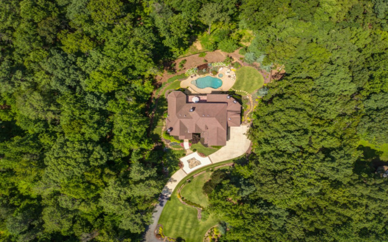 Aerial view of a wooded home with a backyard pool and curved driveway.