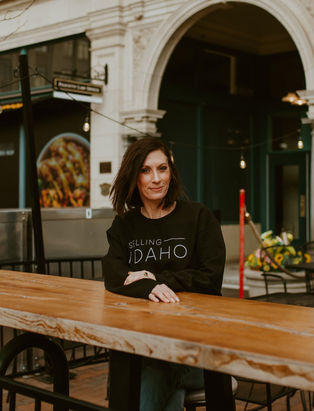 Woman in a Selling Idaho sweatshirt seated at a wooden outdoor table.