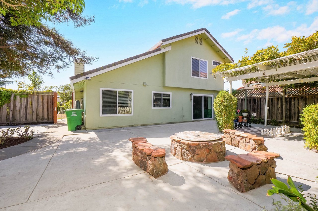 Home’s backyard patio with a circular stone fire pit, built-in seating, and pergola-covered chess area.