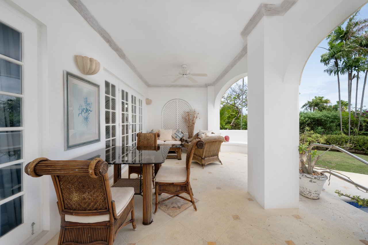 Covered patio with wicker seating, white arches, and a tropical garden view.