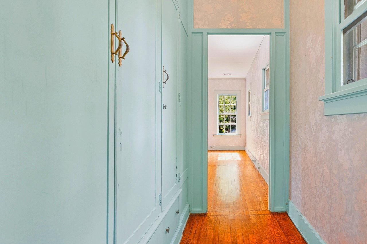 Hallway with mint-green built-ins, pink patterned walls, and polished hardwood floors leading to a bright room.