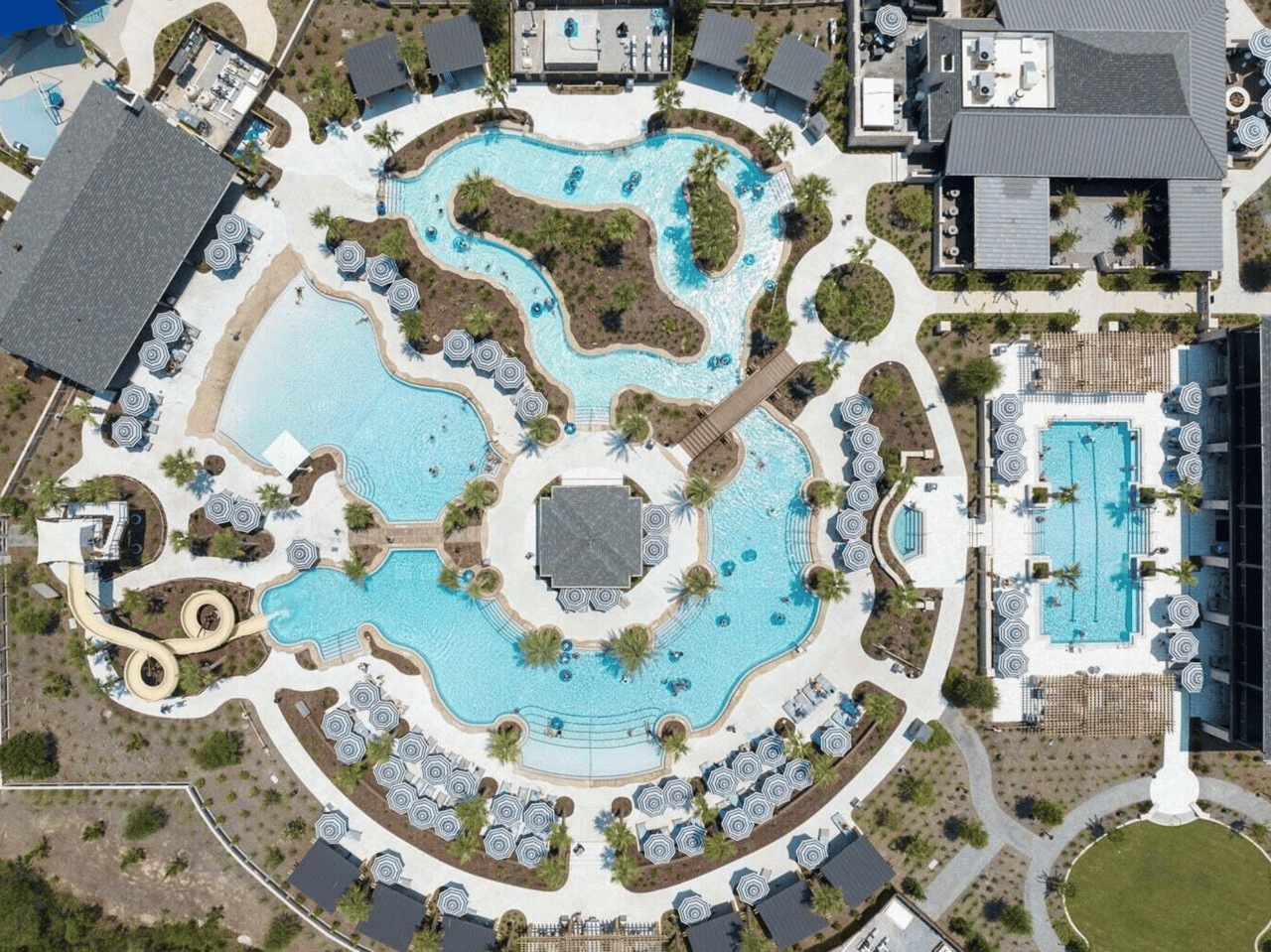 Aerial view of interconnected resort pools with landscaped islands and striped umbrellas.