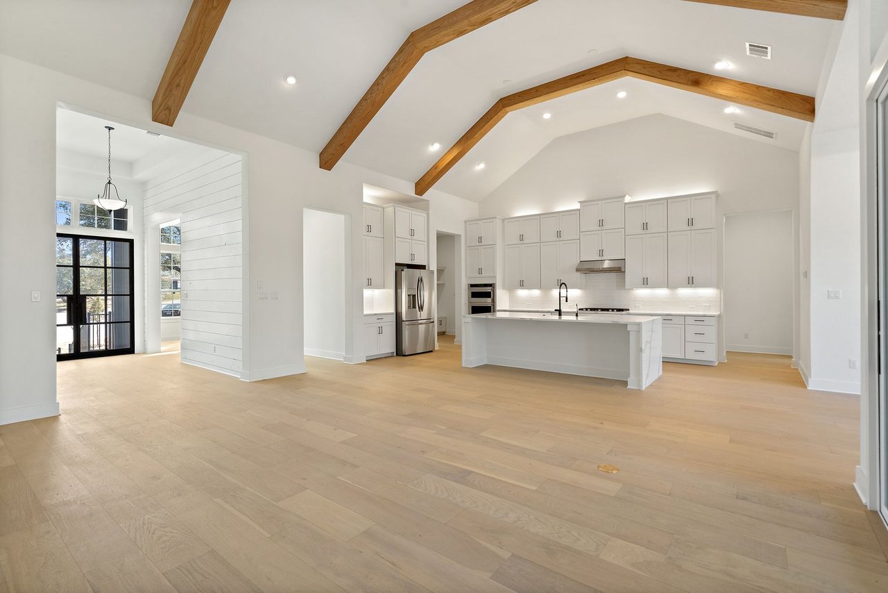 Vaulted great room with exposed wood beams and an open floor plan into the kitchen, in the Cortaro home at 133 Mataro Cove, Dripping Springs, Texas.