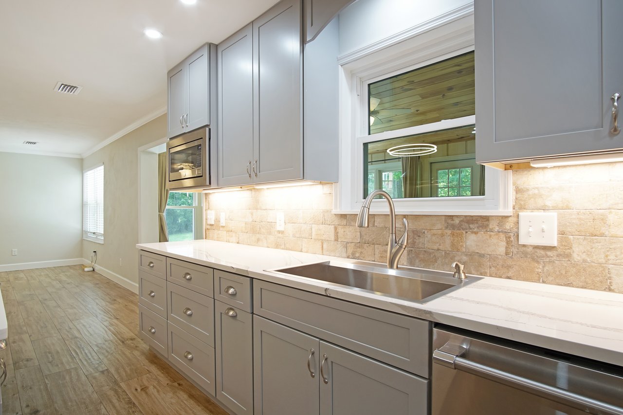 Modern kitchen with gray cabinets, marble countertops, and stainless steel sink. Subway tile backsplash and warm lighting create an inviting ambiance.
