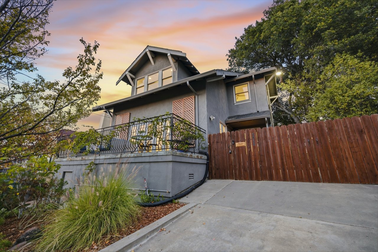 Gray two-story house with a raised balcony and wooden gate at dusk.