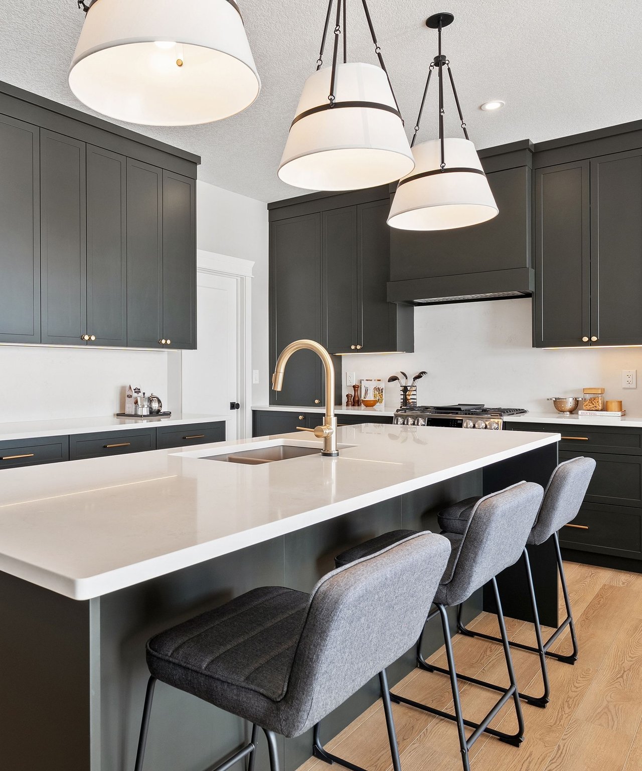 Modern kitchen with dark cabinets, a white island, gold faucet, and three gray bar stools.