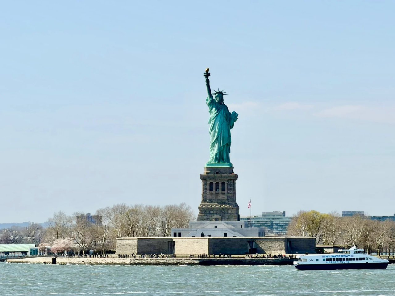 The Statue of Liberty on Liberty Island, with a harbor tour boat passing in the foreground.