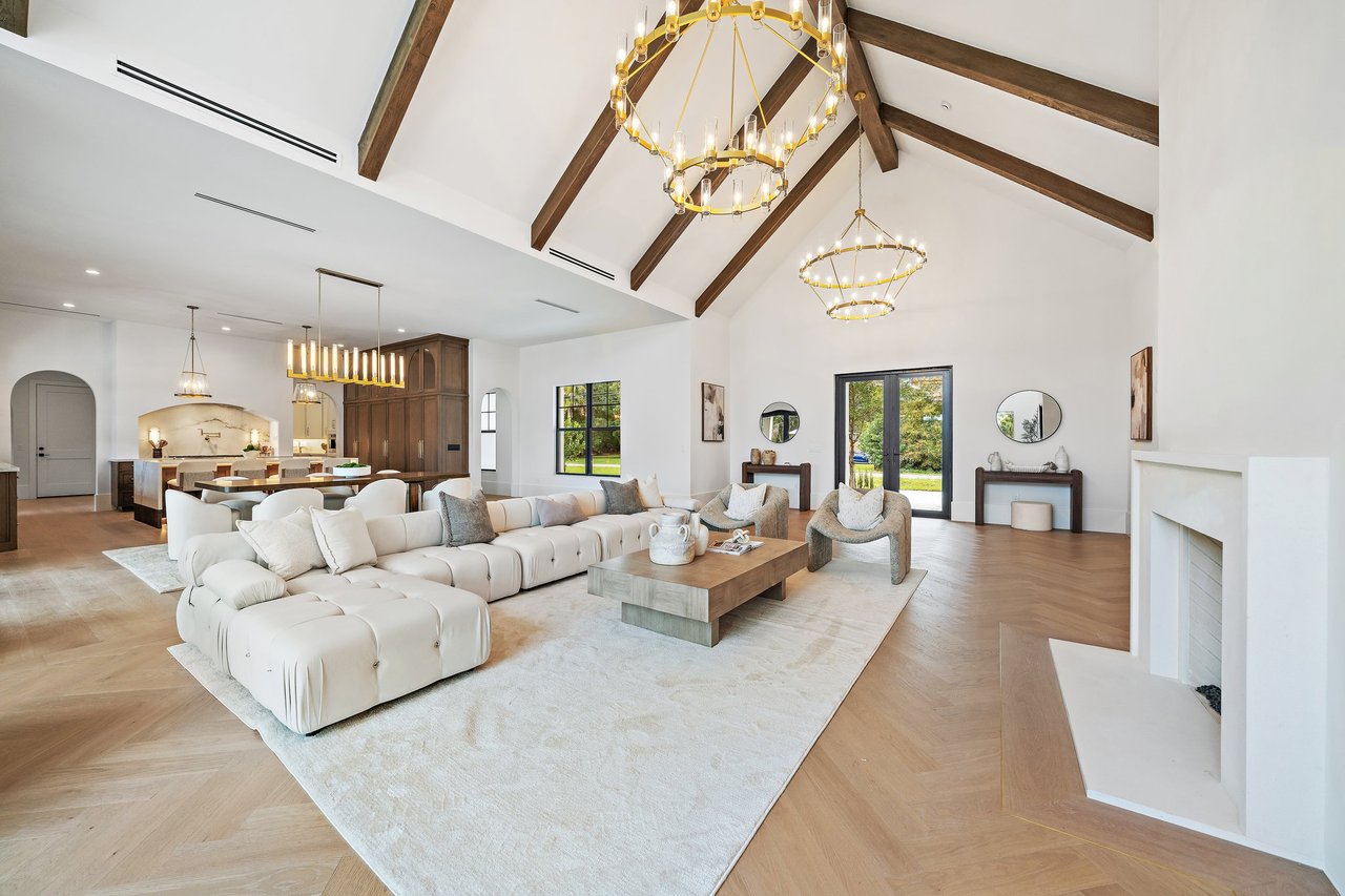 Vaulted living room with exposed wood beams, a white sectional, fireplace, and open dining area.