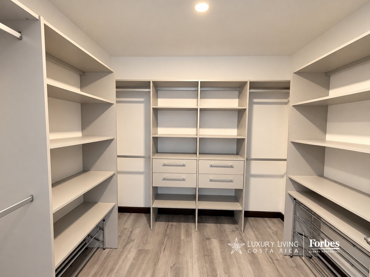 Walk-in closet with extensive built-in shelving, hanging rails, drawers, and wood-look flooring.
