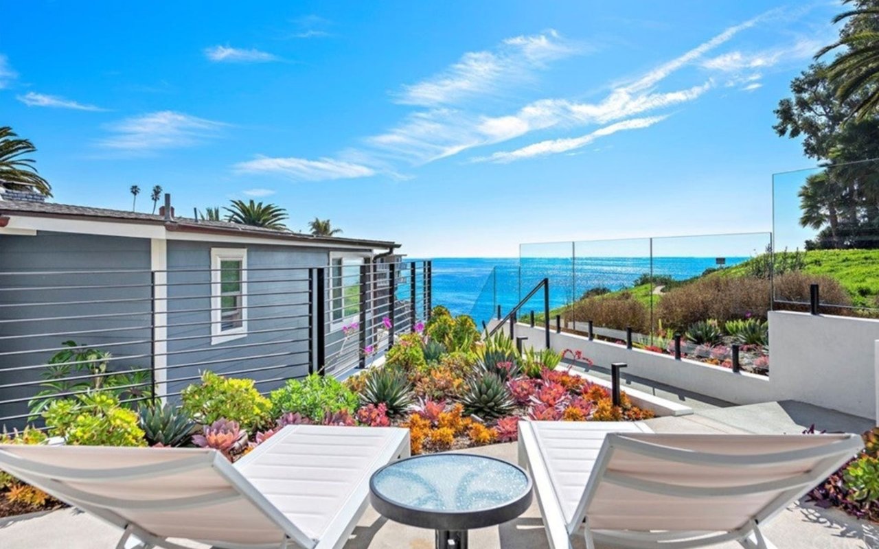 Oceanfront patio with white chaise lounges, colorful succulents, and a view of the water.