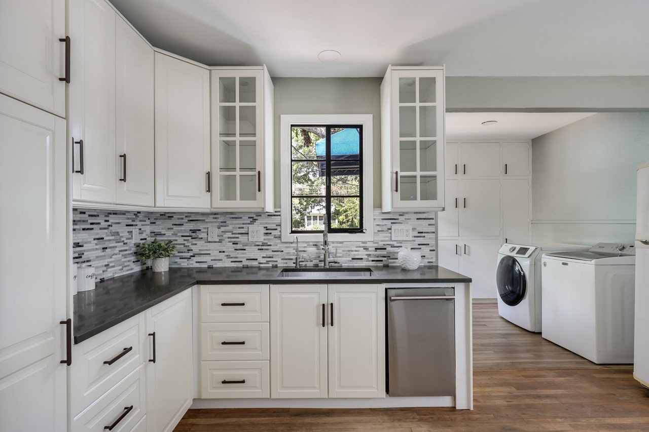 Kitchen with white shaker cabinets, gray mosaic backsplash, dark countertops, and laundry appliances nearby.