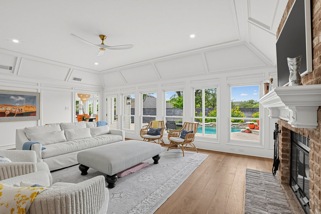 Living room with a coffered ceiling, brick fireplace, and windows overlooking a backyard pool.