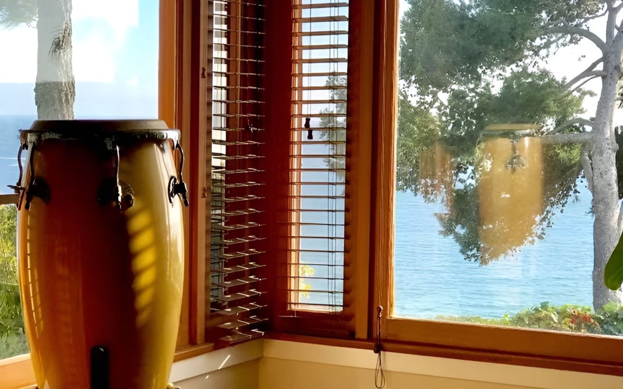 Conga drums beside wood-framed windows overlooking the ocean.