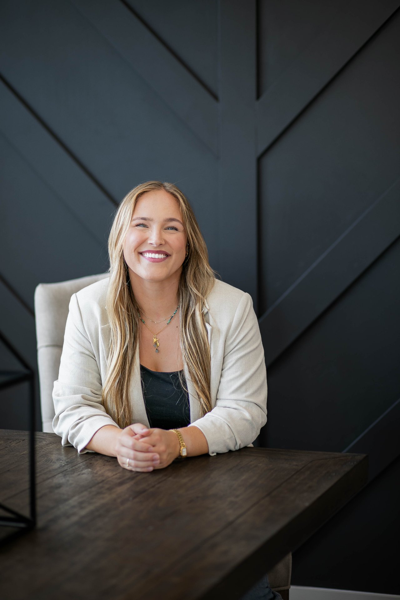 Brianne Beauchamp smiling in a white blazer, seated at a dark wooden table.