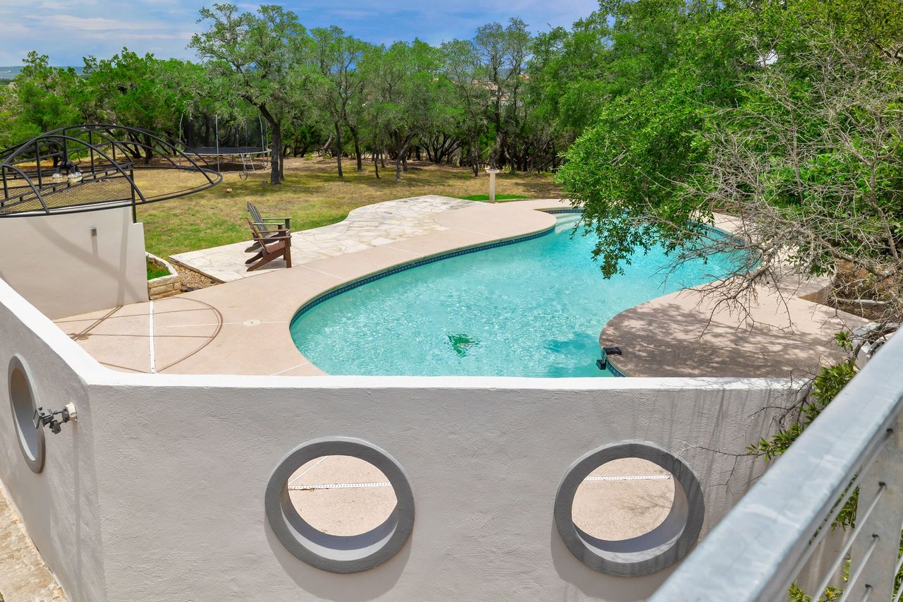 Elevated view of the pool and lawn framed by the home's round porthole windows at 3935 Lago Vista Drive, a hilltop Mid-Century Modern home overlooking Lake Travis in the Highland Club Village area of Austin, TX.